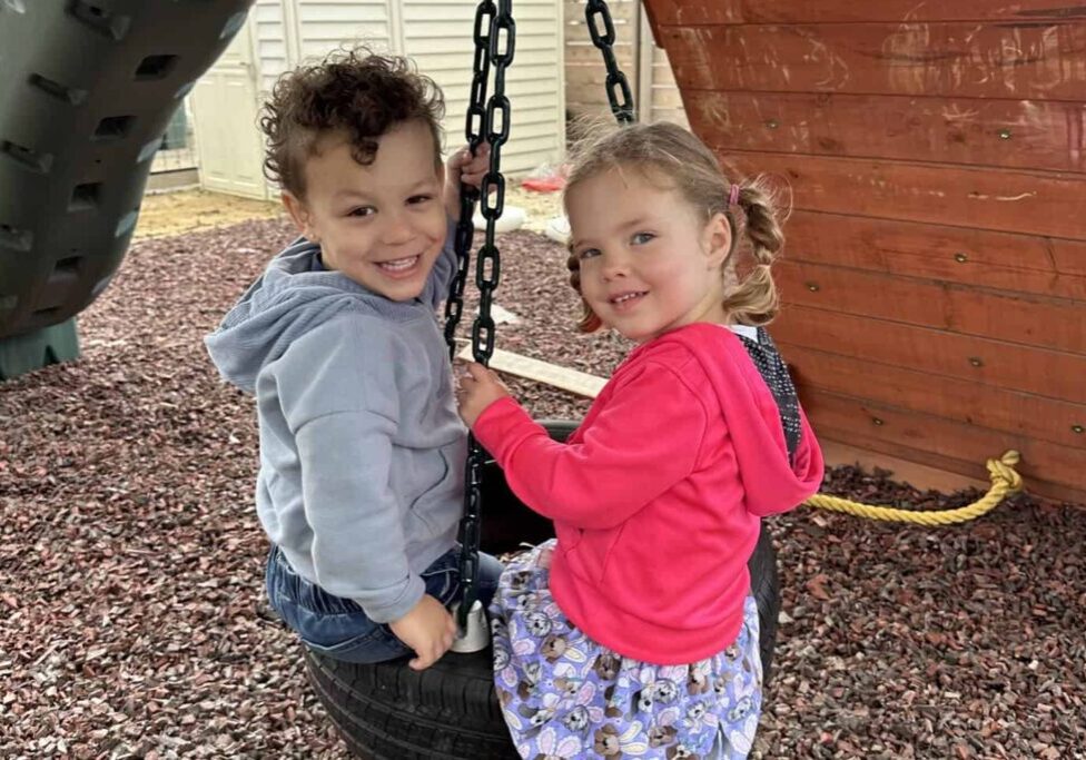 Two preschool-aged children swing together in a tire swing.