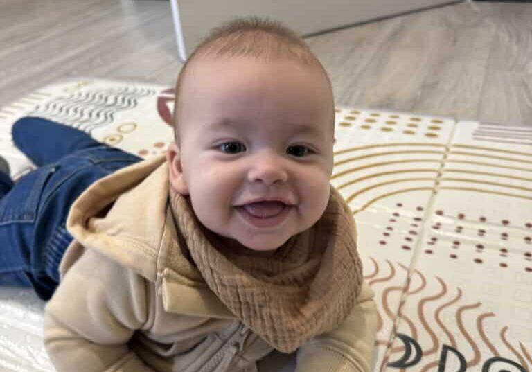 A smiling infants plays on his tummy on a blanket